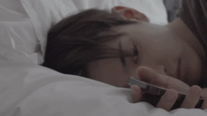 Man looking lying on the bed, holding the phone in the hand, looking depressed. The scene is a part of the song: “Why Do You Love” By Ateez Hongjoong
